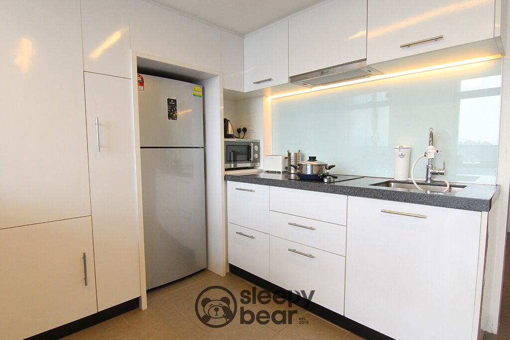 Una cocina moderna con armarios blancos, microondas integrado y refrigerador de acero inoxidable.