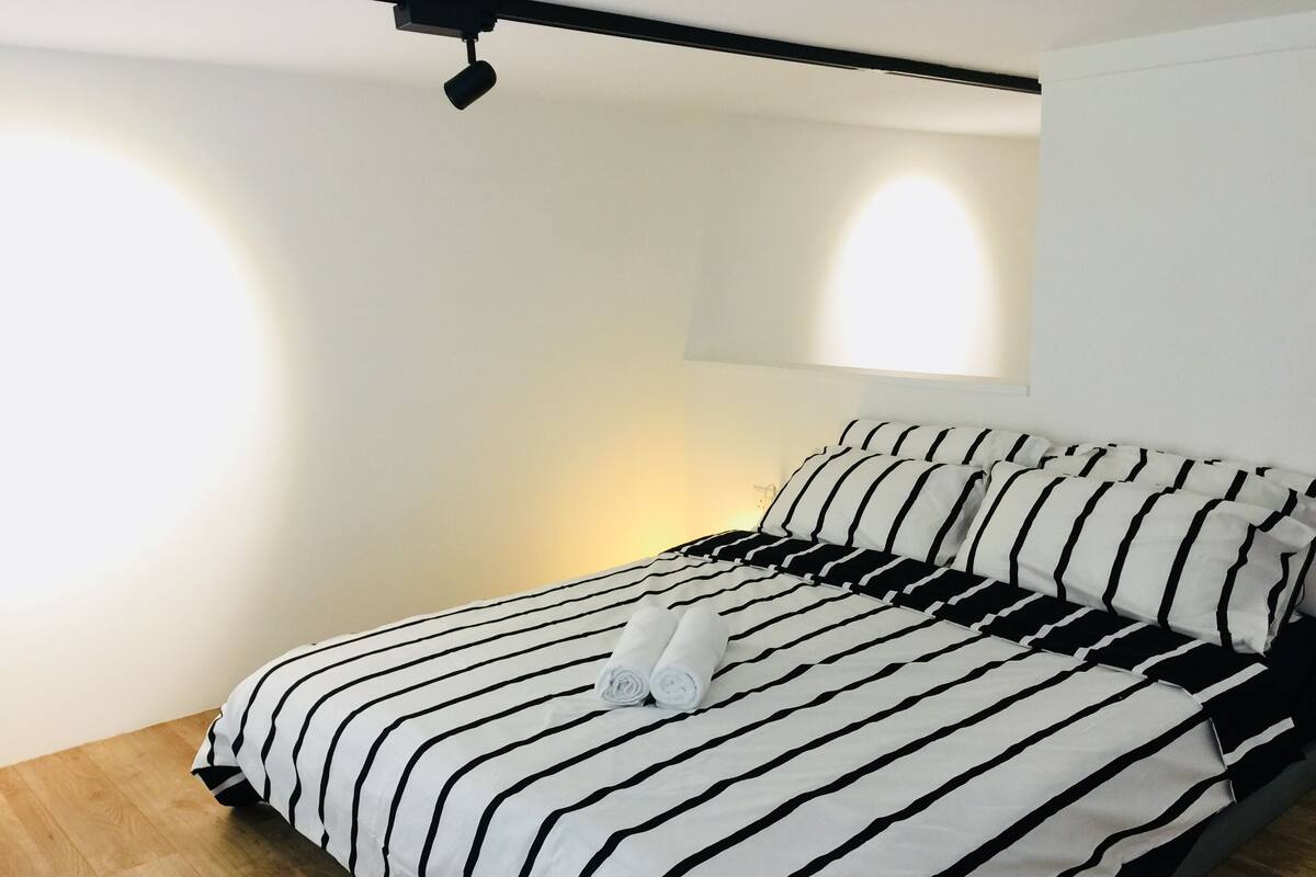 A neatly made bed with black and white striped bedding, a rolled towel, and a ceiling-mounted light fixture.
