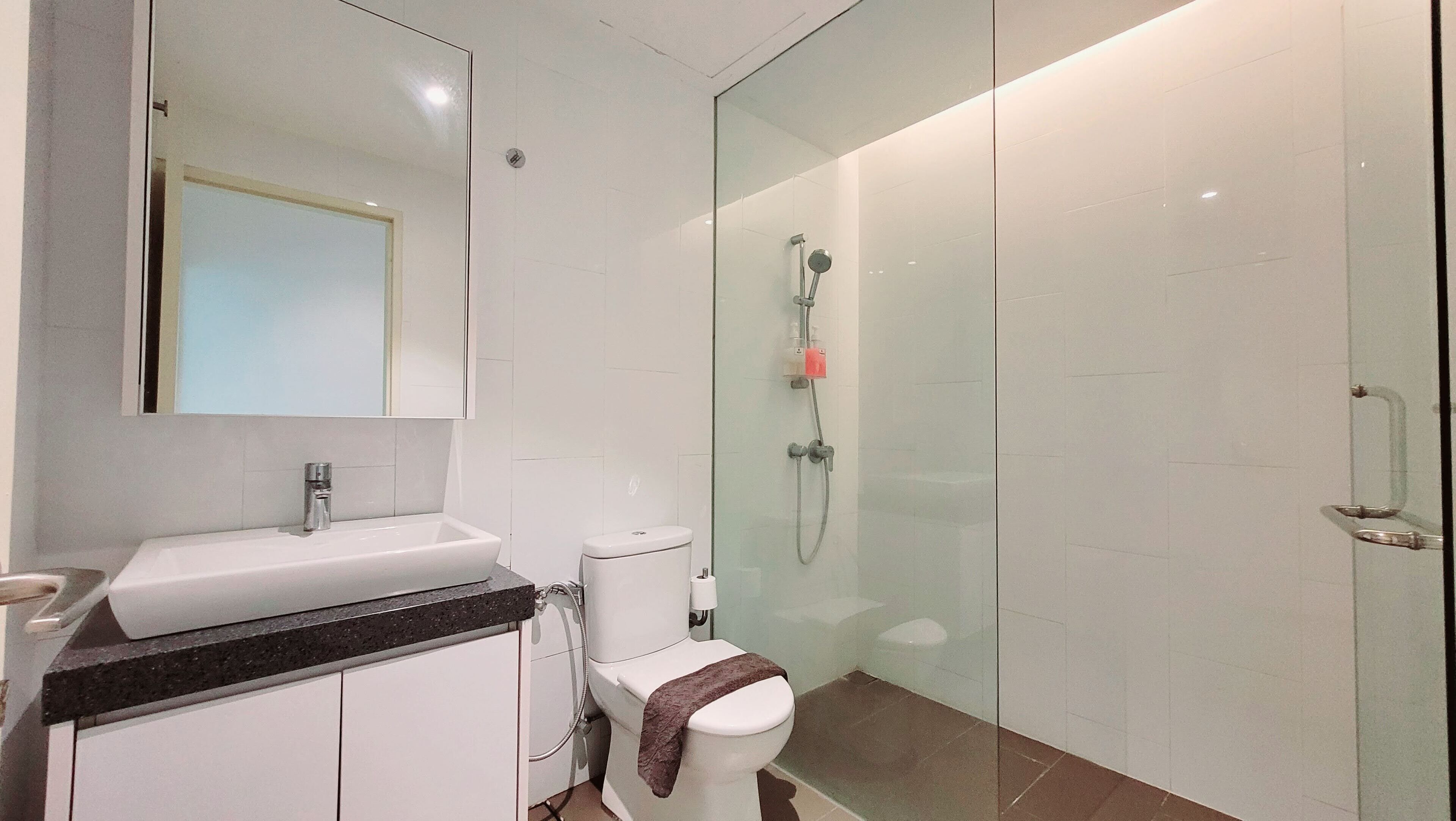 Un bany modern amb plat de dutxa envoltat de vidre, un lavabo blanc i un vàter.