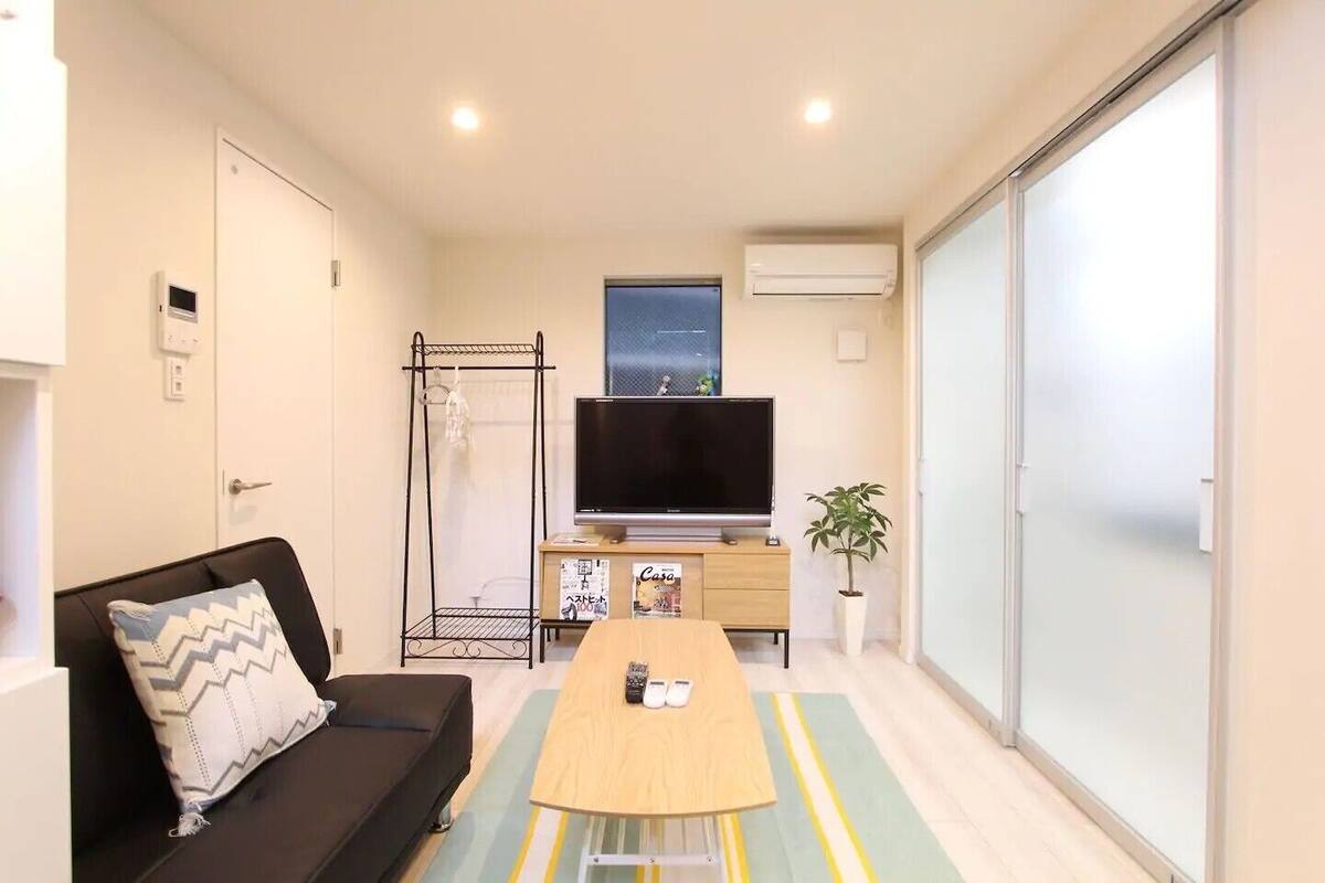 Un espacio habitable compacto con sofá, televisor, una mesita, una planta y una puerta corredera.