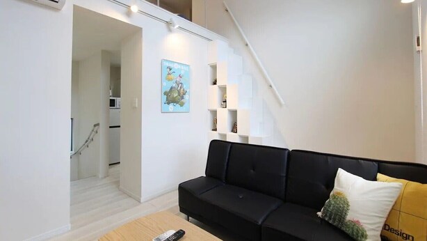 A modern living room with a black sofa, a remote control on a wooden coffee table, and a staircase leading to an upper level. - Shibuya Stay Tokyo (Tokyo)
