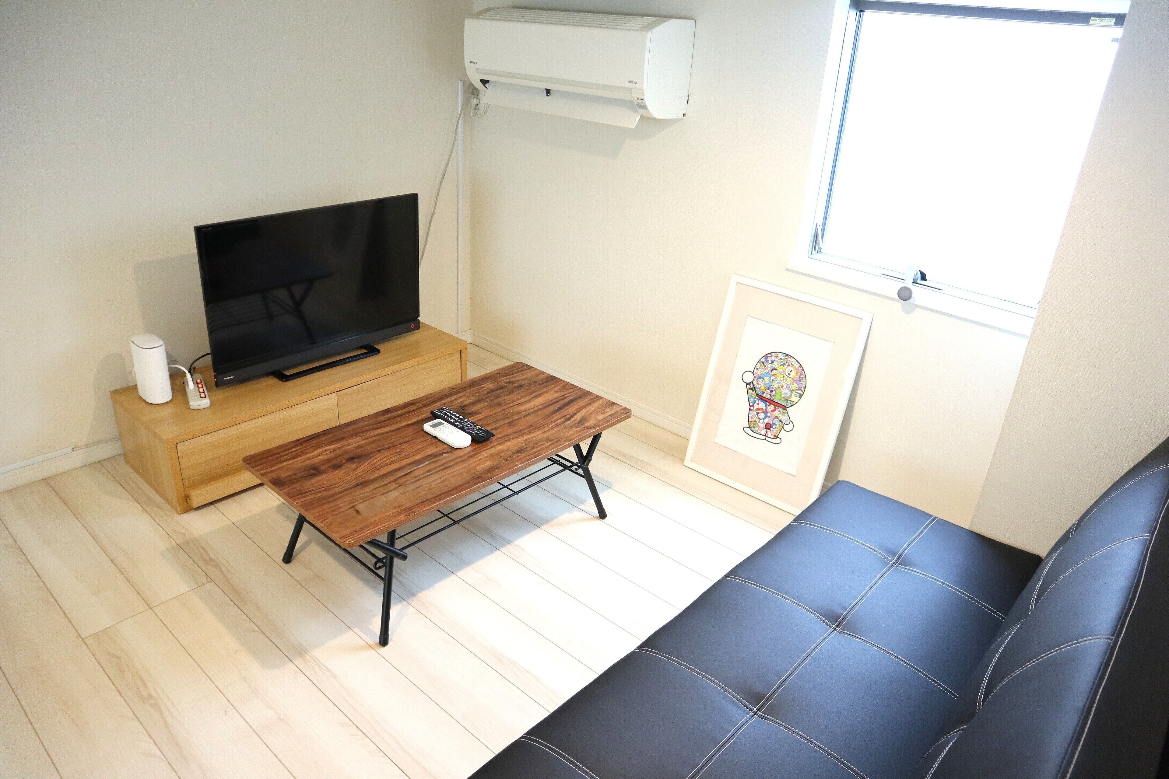 A living room with a flat-screen TV, a wooden coffee table, a black sofa, a framed picture, and a window with blinds.