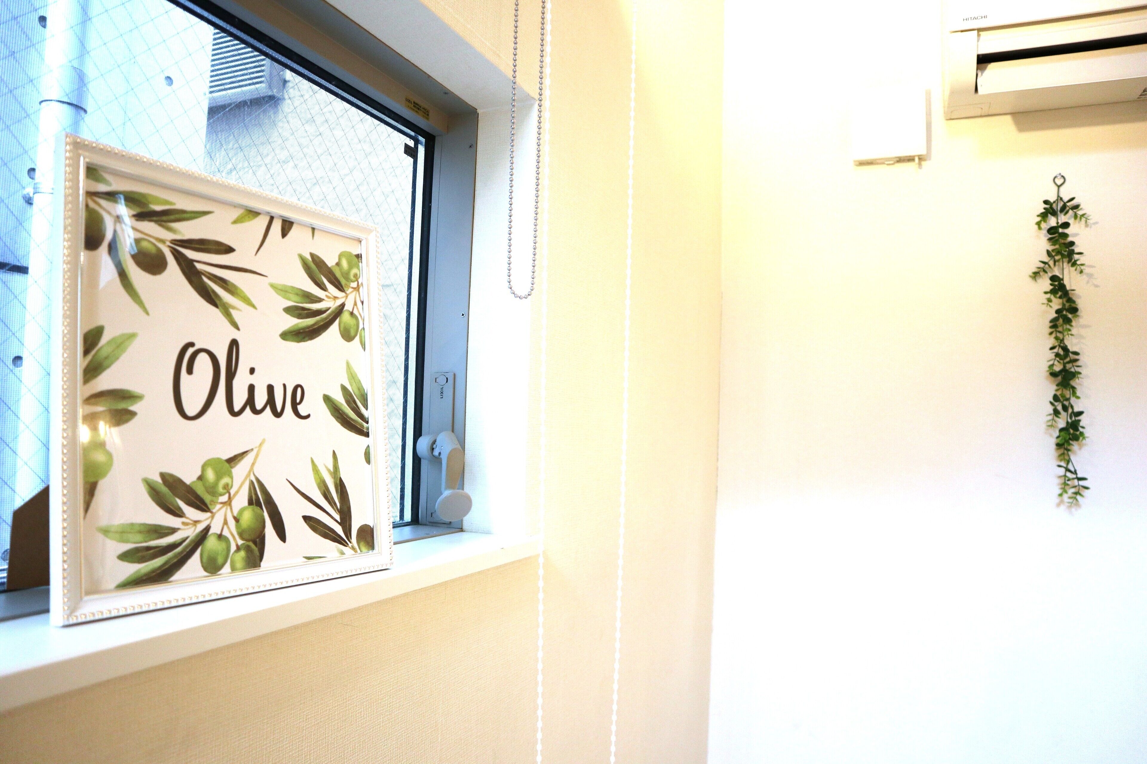 A framed picture with the word "Olive" and olive branches on a window sill.