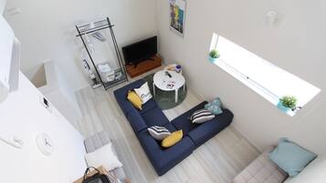 A modern living room with a blue sofa, a small round table, a TV, and a window with a plant.