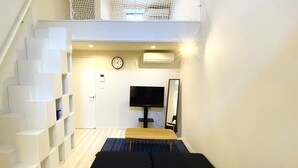 A compact hotel room with a bed, a TV, a mirror, and a staircase with storage units. - Shibuya Stay Tokyo (Tokyo)