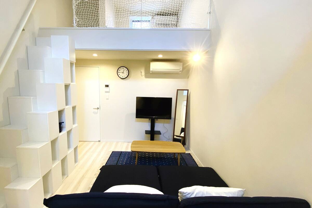 Una habitación de hotel compacta con cama, televisión, espejo y una escalera con espacios de almacenamiento.