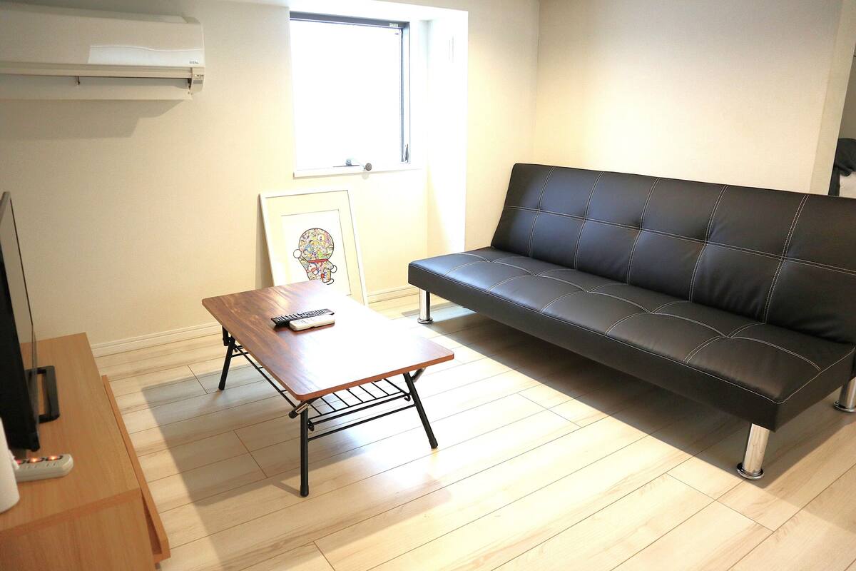 Una sala de estar con un sofá de cuero negro, una mesa de centro de madera y un cuadro enmarcado en la pared.
