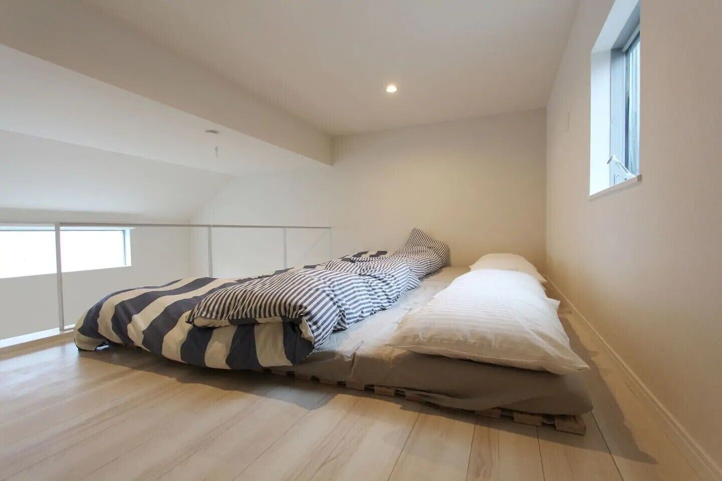 A bedroom with a bed, striped bedding, a window, and a wooden floor.