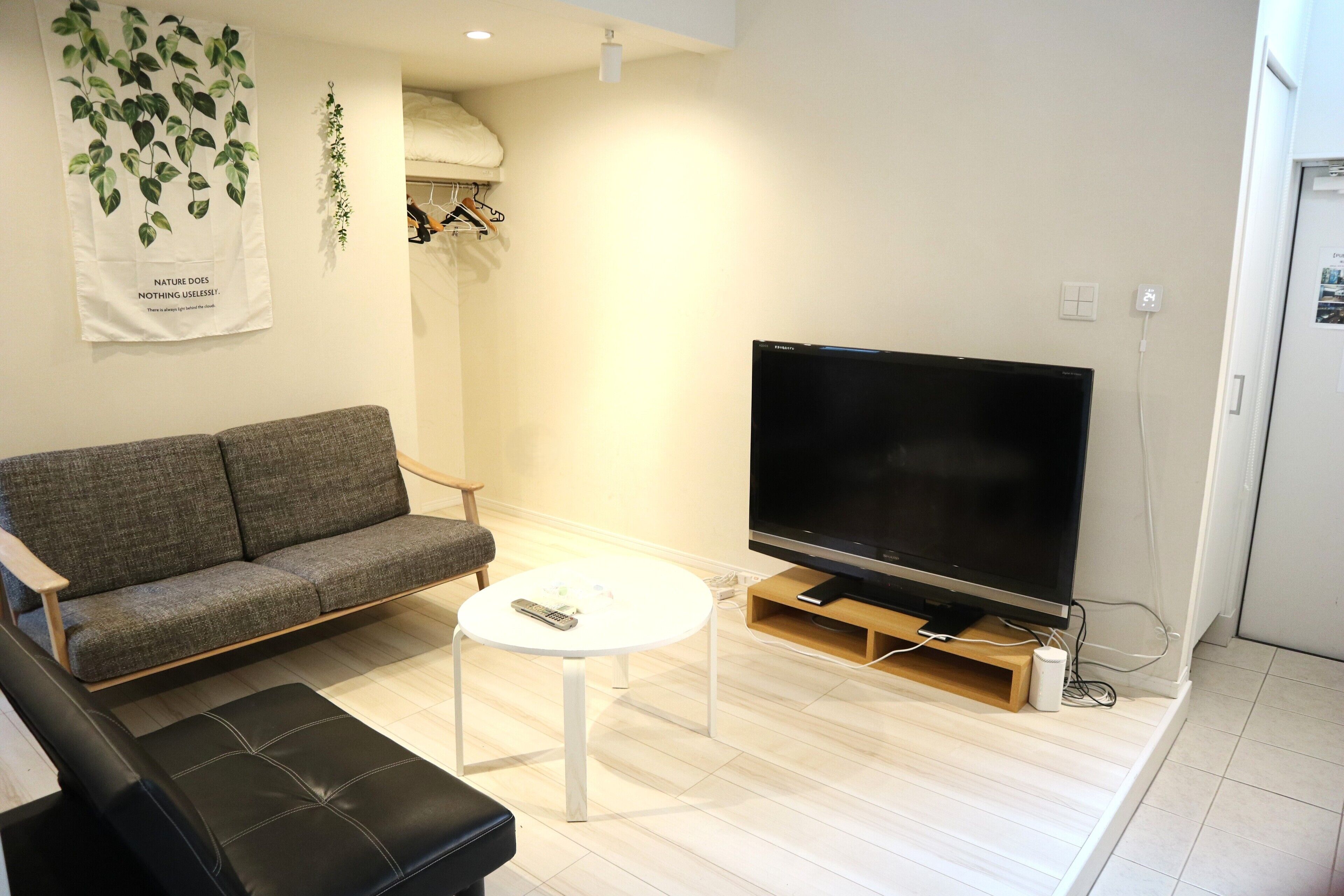 A living room with a grey sofa, a black leather chair, a white coffee table, and a flat-screen TV on a wooden stand.