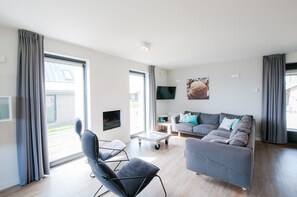 A modern living room with a sofa, a chair, a flat-screen TV, and a sliding glass door. - Villa Oesterdam Sleeps 8 Persons (Tholen)