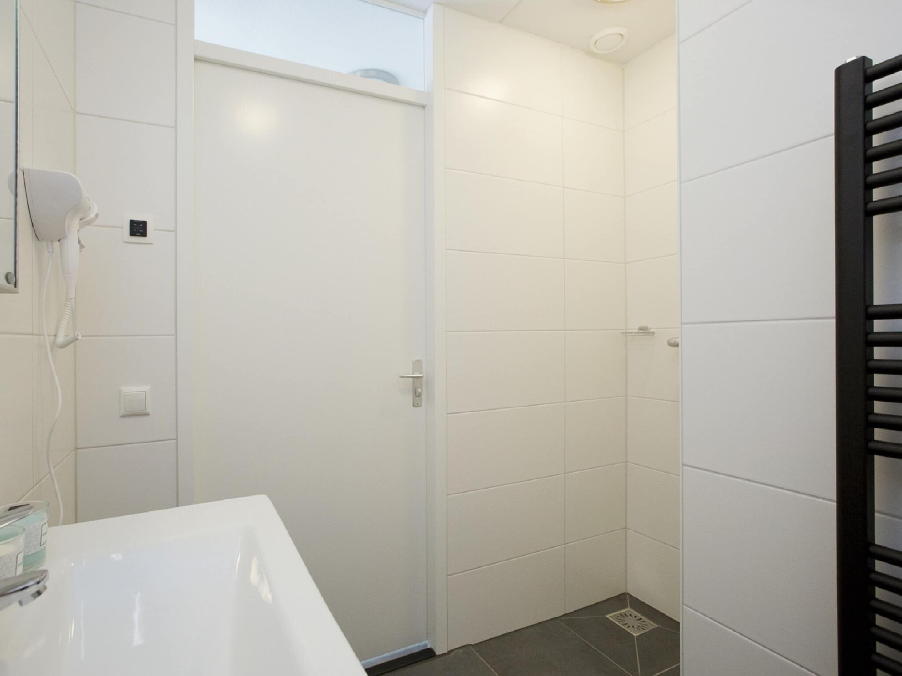 A bathroom with a white sink, a shower area, and a black towel rack.