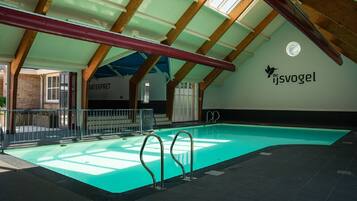 An indoor swimming pool with a high ceiling and wooden beams, a visible water slide, and a sign reading "de ijsvogel".