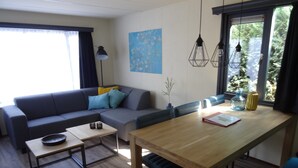 Una sala de estar moderna con un sofá, una mesa de comedor y una mesa de centro. Hay una ventana con cortinas, una lámpara de pared y un cuadro.