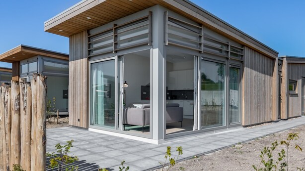 Una casa moderna con amplios ventanales, una terraza de madera y un cielo azul despejado.