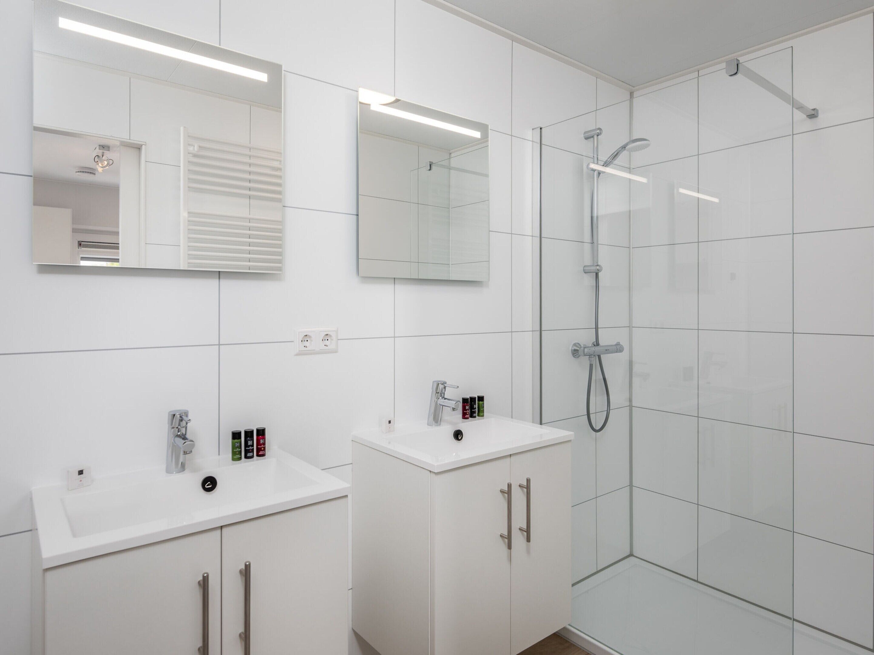 Un baño moderno con dos lavamanos, ducha y espejo.