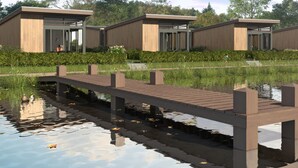 Un edificio moderno con fachada de madera y grandes ventanales, ubicado junto a una masa de agua con un puente de madera.