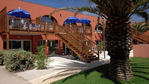 Un hotel con balcón de madera, sombrillas azules y una palmera.