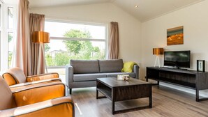 A modern living room with a sofa, armchair, coffee table, TV, and artwork on the wall. - Comfortable Chalet With Dishwasher in Noordwijk (Noordwijk)