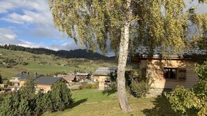 Paisagem rural com casas, uma árvore grande e uma montanha ao fundo.