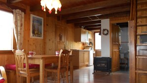 Interior em madeira com mesa de jantar, cadeiras, cozinha e lareira.
