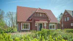 Ein zweigeschossiges Haus mit rotem Ziegeldach, einer Veranda und einem gepflegten Garten.
