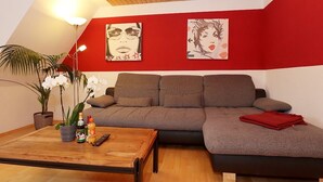 A modern living room with a wooden ceiling, red walls, and a sectional sofa. There is a coffee table with a plant and a bottle. - Gemutliche Wohnung in Schwenningen (Villingen-Schwenningen)