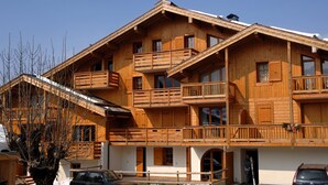 Un edificio de madera de varios pisos con balcones, un telesilla y un coche estacionado adelante.