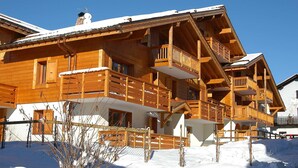 Una cabaña de madera con varios balcones, techo cubierto de nieve y entrada protegida por una cerca.