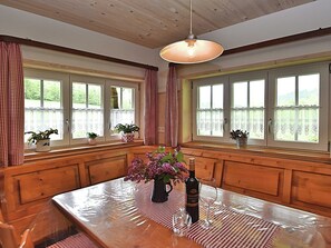 Una mesa de comedor de madera con una botella de vino y copas, rodeada de ventanas con cortinas.