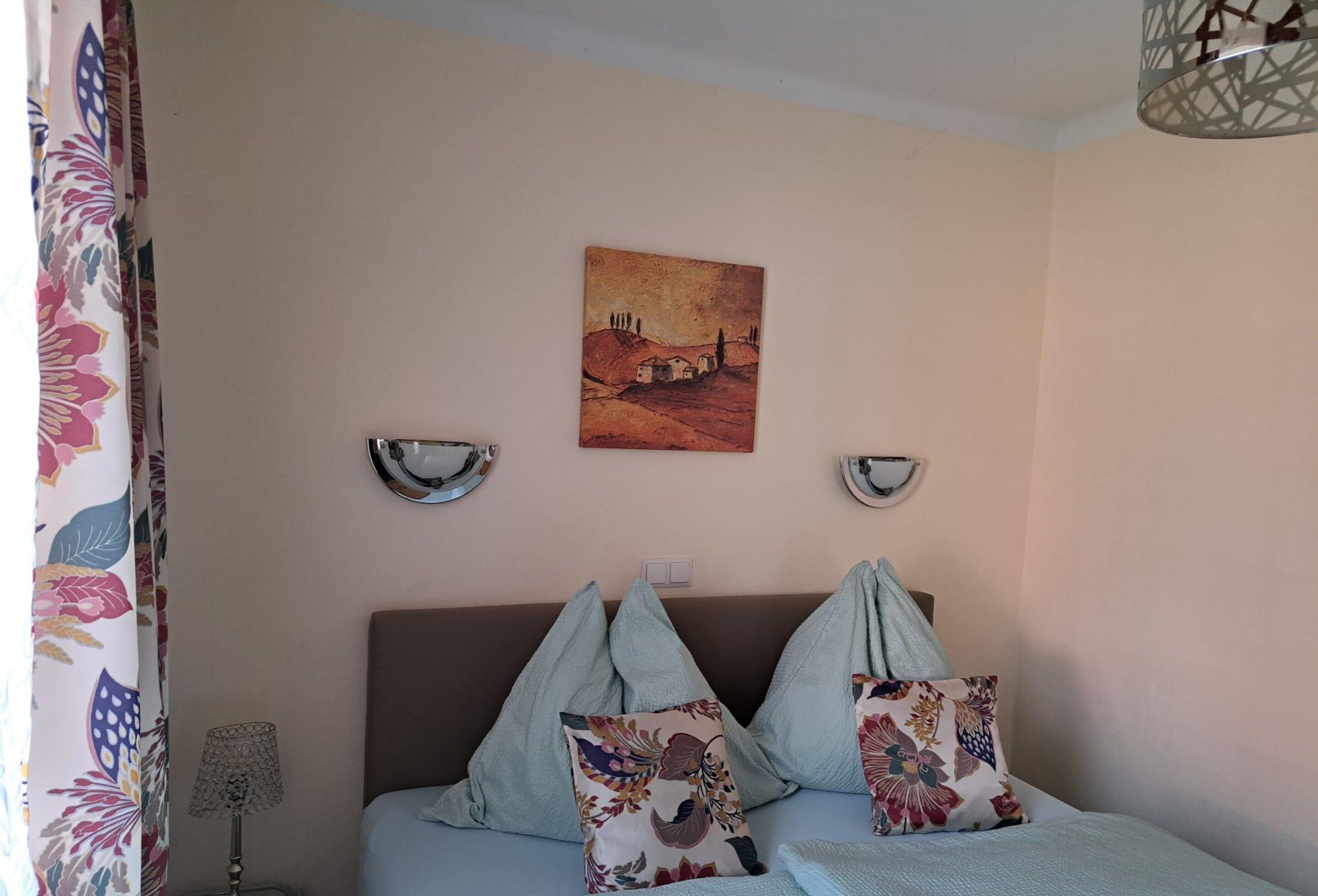 Een slaapkamer met een bed, twee wandlampen, een schilderij en een gordijn met een bloemendesign.