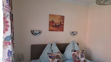 Een slaapkamer met een bed, twee wandlampen, een schilderij en een gordijn met een bloemendesign.