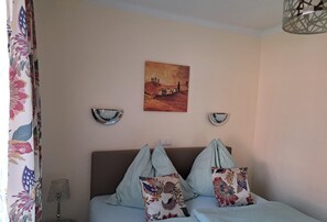 Een slaapkamer met een bed, twee wandlampen, een schilderij en een gordijn met een bloemendesign.