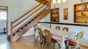 A dining area with a wooden staircase, a striped tablecloth-covered table, and wooden chairs. - Spacious Chalet in Maishofen near Forest (Maishofen)