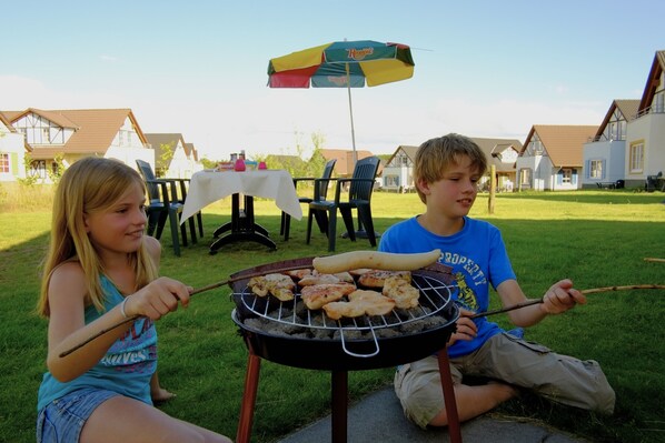 Two individuals grilling outdoors with a table and chairs in the background. - Restyled Villa with Washing Machine near River Moselle (Ediger-Eller)