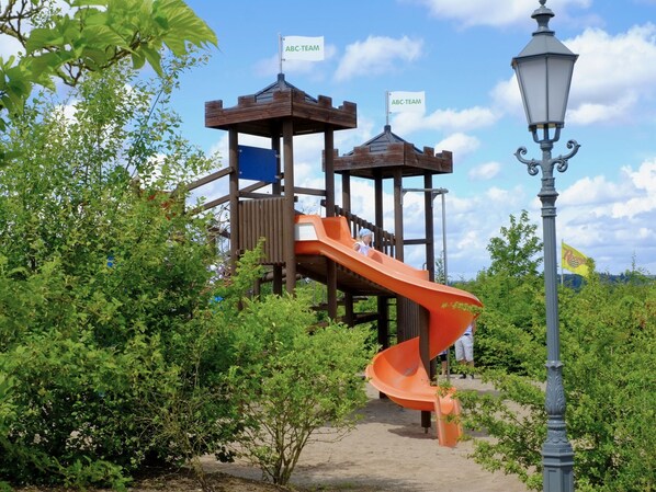 A playground with a slide and two wooden playhouses, surrounded by greenery. - Restyled Villa with Washing Machine near River Moselle (Ediger-Eller)