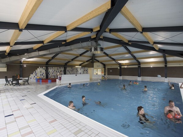 Swimmers enjoy the pool surrounded by a spacious area with seating and tables.