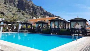 Un área de piscina con agua azul cristalina, rodeada de edificios y una ladera rocosa.
