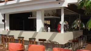 Un área de bar al aire libre con sillas y mesas de madera, una barra con botellas y un ventanal grande.