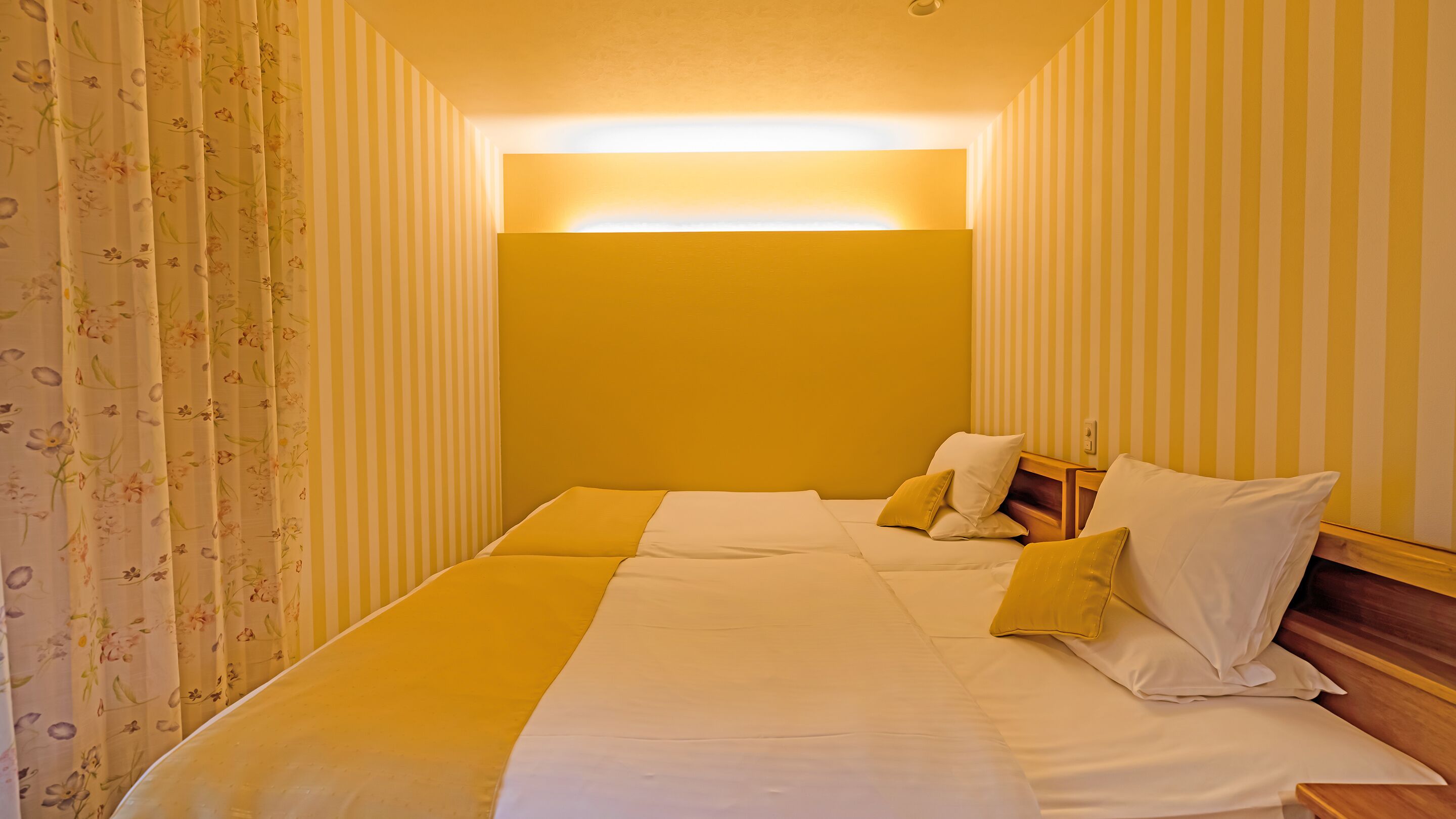 A hotel room with a bed, pillows, and striped wallpaper.