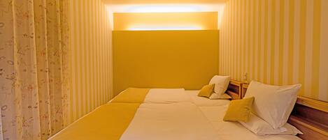 A hotel room with a bed, pillows, and striped wallpaper.