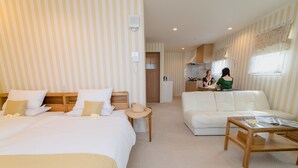 A hotel room with two beds, a sofa, a wooden coffee table, and a kitchen area visible through an open door. - Ecot Shimozato 3 (Miyakojima)