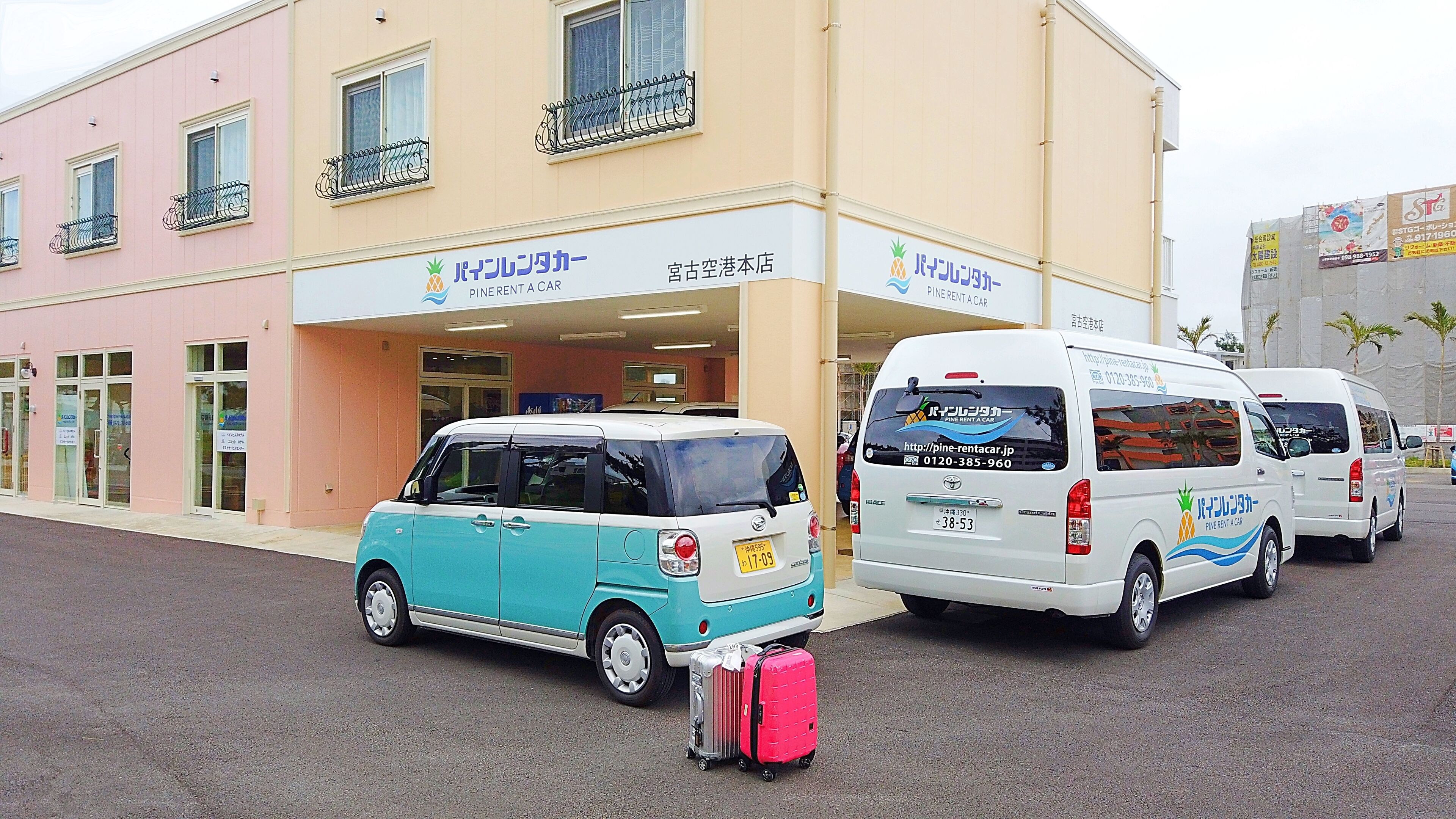 Un bâtiment avec une enseigne indiquant « Pine Rent a Car ». Deux fourgonnettes blanches sont garées devant, avec des bagages à l’intérieur.