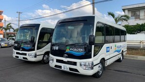 Two white minibuses parked in a lot with a clear sky and buildings in the background. - Ecot Shimozato 3 (Miyakojima)