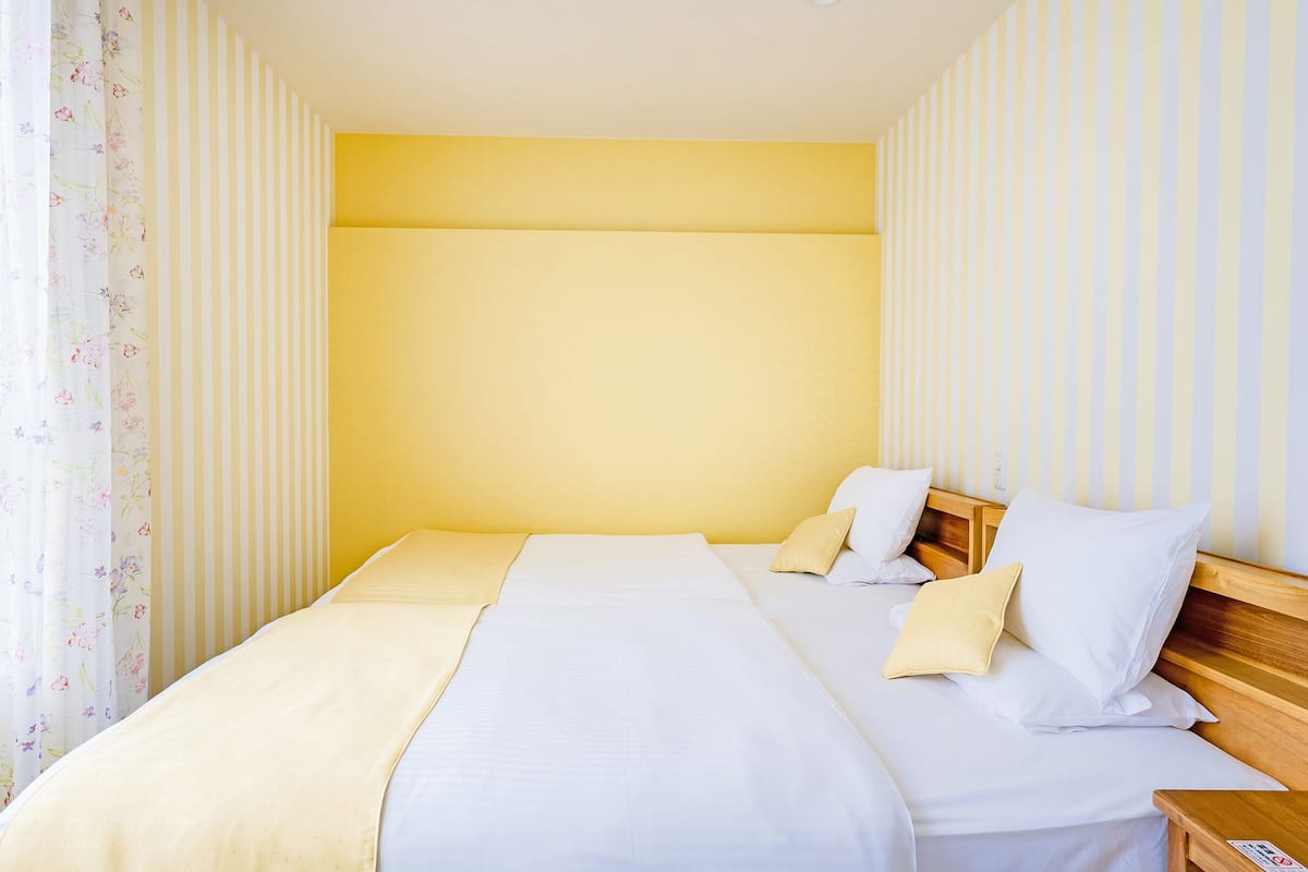 A neatly made bed with white and beige bedding, a wooden headboard, and a bedside table with a lamp.