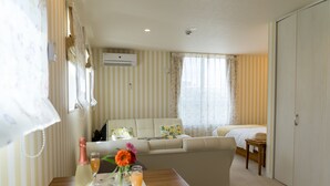 A hotel room with a sofa bed, a small table with a bottle and glasses, and a window with curtains. - Ecot Shimozato 3 (Miyakojima)