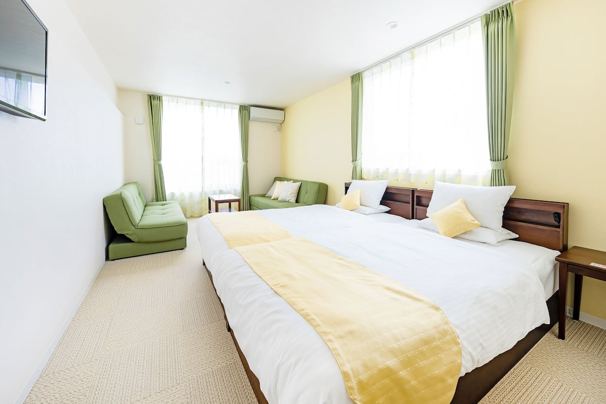 A hotel room with a large bed, a green sofa, and a small table.