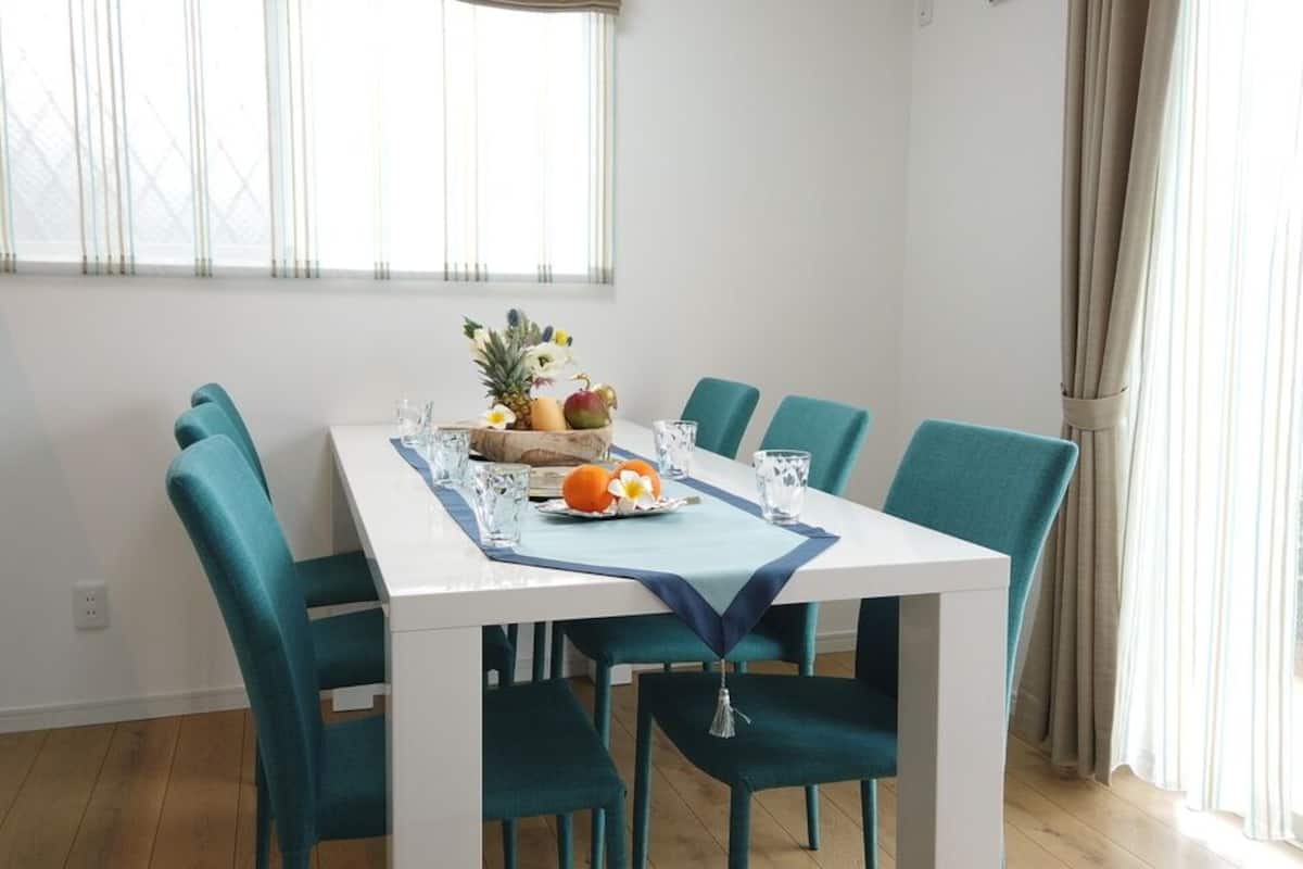 A dining table with six teal chairs, a fruit bowl, and a vase with flowers on the table.