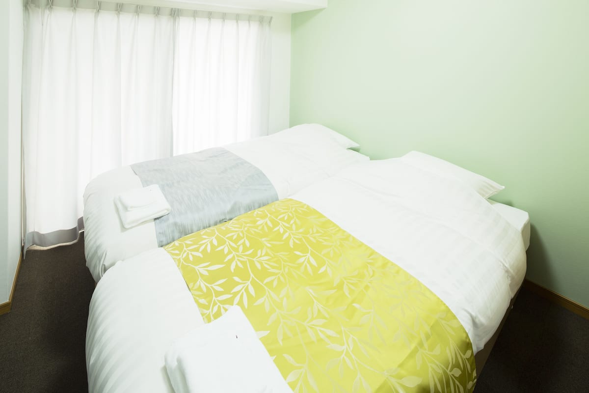 A hotel room with two beds, a window with curtains, and a green wall.