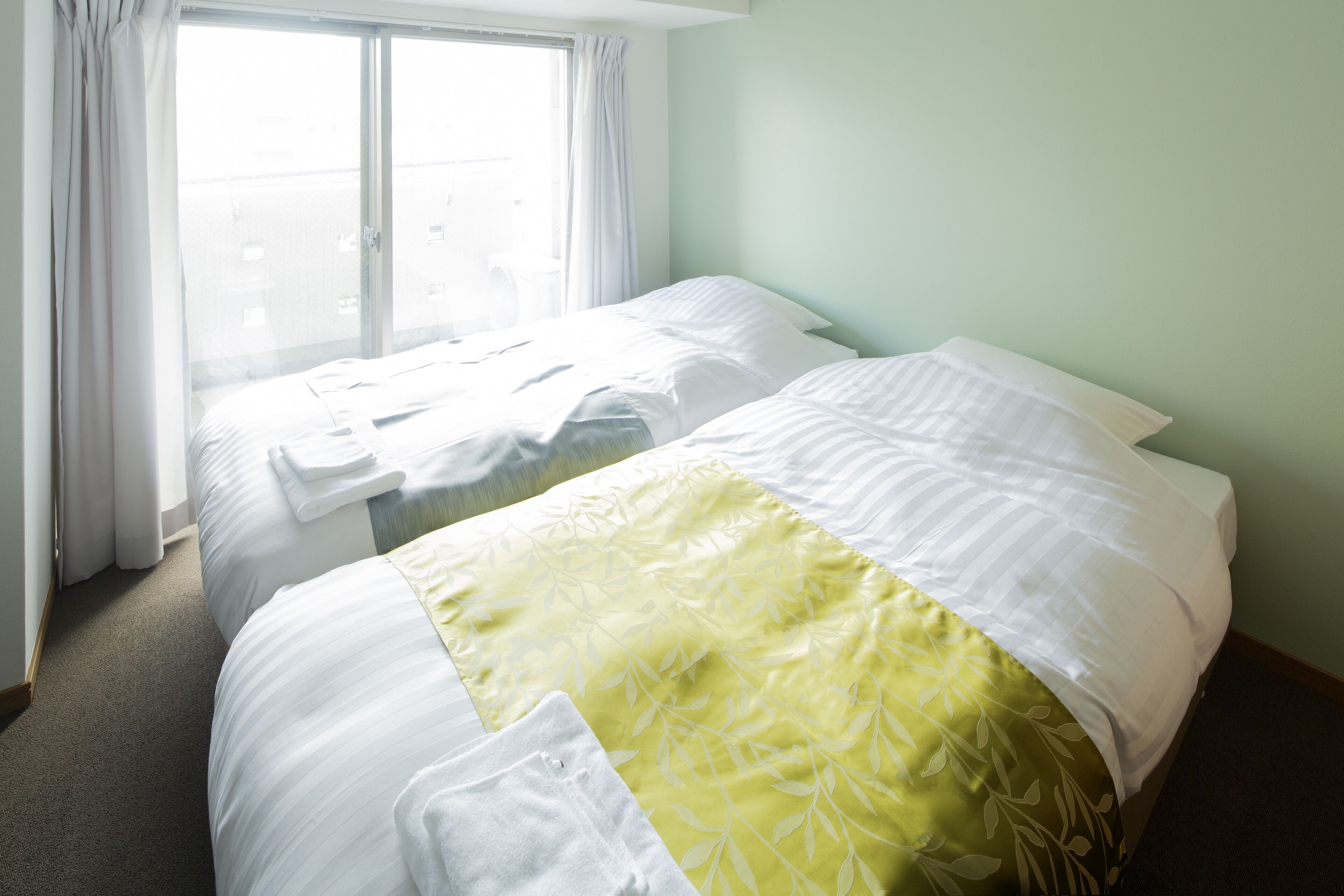 A hotel room with two beds, a large window with curtains, and a green wall.