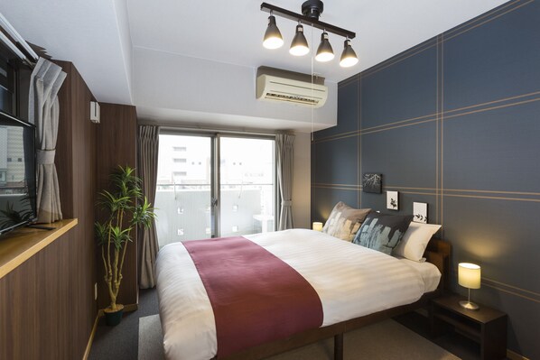 A modern hotel room with a large bed, a bedside table with a lamp, a potted plant, and a view of the city through the window. - Coruscant Hotel Nagasaki Station (Nagasaki)